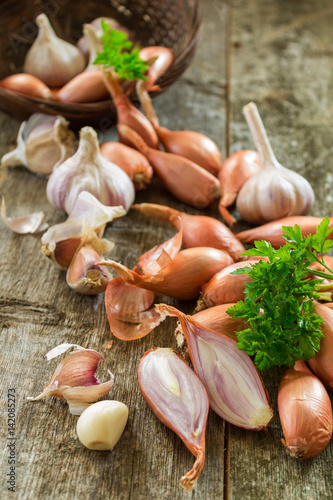 Scattered from wicker basket of garlic and onions, shallots peeled sliced with green leaves of parsley on a wooden background close-up. Rural scene. Vertical photo