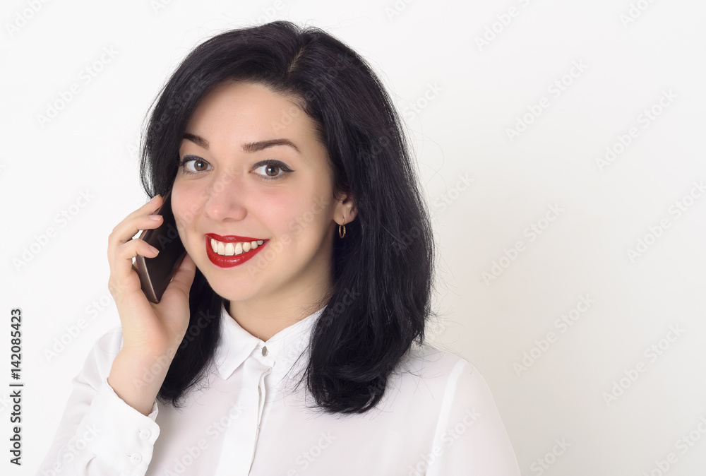 Beautiful business woman in a white blouse and with bright red lipstick on her lips talking on her mobile phone. She smiles a snow-white smile and enjoys a successful conversation. Beautiful business woman in a white blouse and with bright red lipstick on her lips talking on her mobile phone. She smiles a snow-white smile and enjoys a successful conversation.