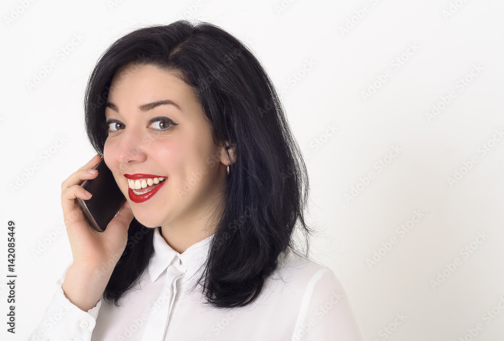 Beautiful business woman in a white blouse and with bright red lipstick on her lips talking on her mobile phone. She smiles a snow-white smile and enjoys a successful conversation. Beautiful business woman in a white blouse and with bright red lipstick on her lips talking on her mobile phone. She smiles a snow-white smile and enjoys a successful conversation.