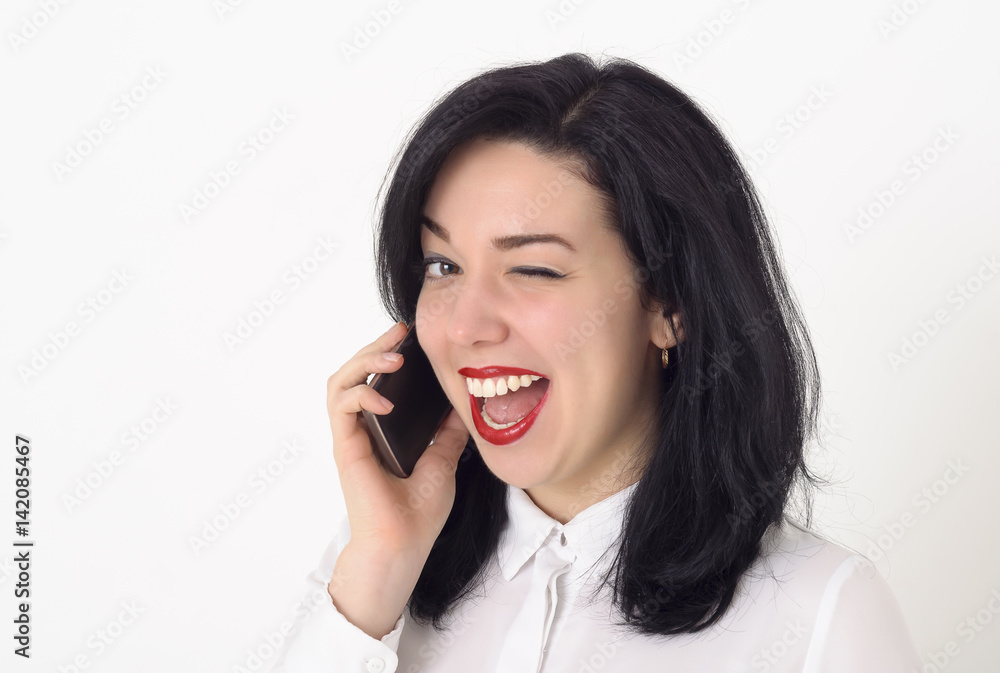 Beautiful business woman in a white blouse and with bright red lipstick on her lips talking on her mobile phone. She smiles a snow-white smile, winks and enjoys a successful conversation. Beautiful business woman in a white blouse and with bright red lipstick on her lips talking on her mobile phone. She smiles a snow-white smile, winks and enjoys a successful conversation.