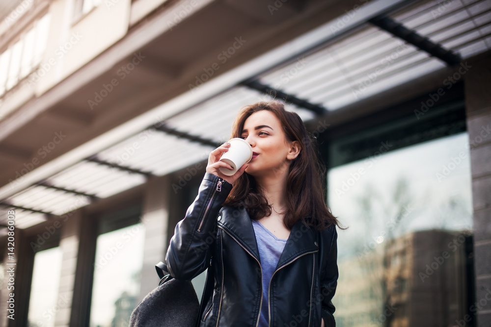 Close up fashion street style portrait of a beautiful girl in a casual outfit walks in the city . Beautiful brunette Keeps coffee. Close up fashion street style portrait of a beautiful girl in a casual outfit walks in the city . Beautiful brunette Keeps coffee.
