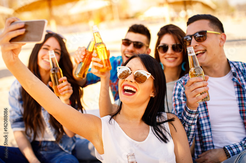 Canvas-taulu Happy young people having fun on the beach drinking beer and doing selfie
