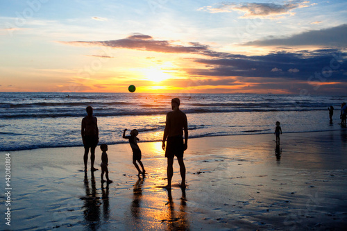 Children and adults play ball on the beach during sunset