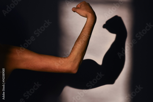 Men's muscles, reality and expectation. Sports and training in the gym. Man's hand and a shadow on the wall. Expectation vs reality photo