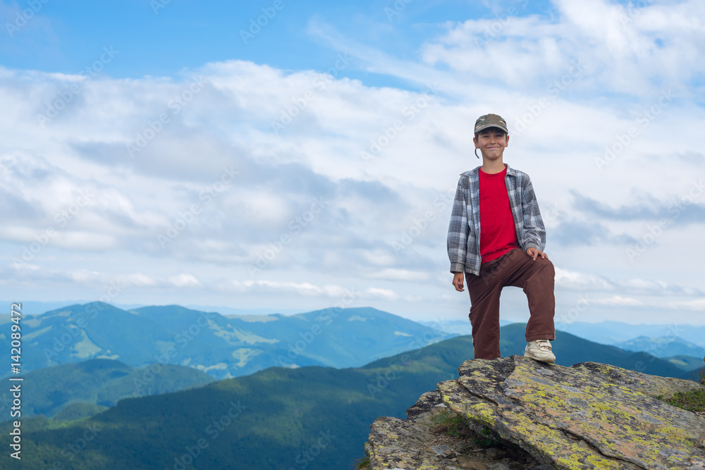 Smiling boy stands on the cliff in the mountain