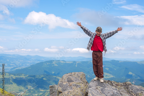 Joyful boy with open arms stands on the cliff in the mountain