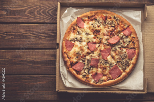 Top view of pizza in a box on wooden table with Mozzarella cheese, ham
