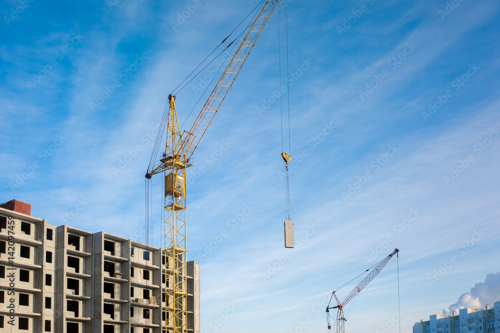 Construction of a new high floor house, using an industrial crane, concrete slabs, building on a blue sky background Construction of a new high floor house, using an industrial crane, concrete slabs, building on a blue sky background