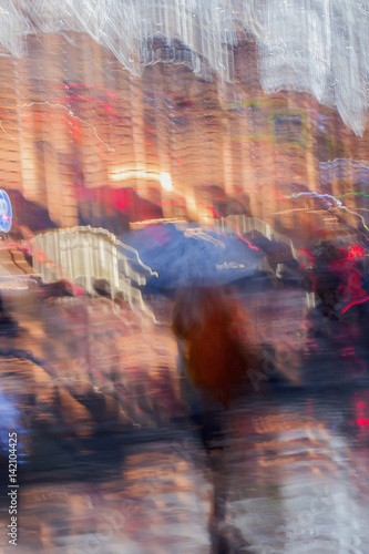 Abstract background of Lonely Girl under umbrella in the, street in rain. Light illumination from lanterns, shop windows. Impressionism style. Intentional motion blur