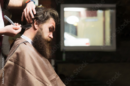 Bearded man with long beard getting hair shaving with razor