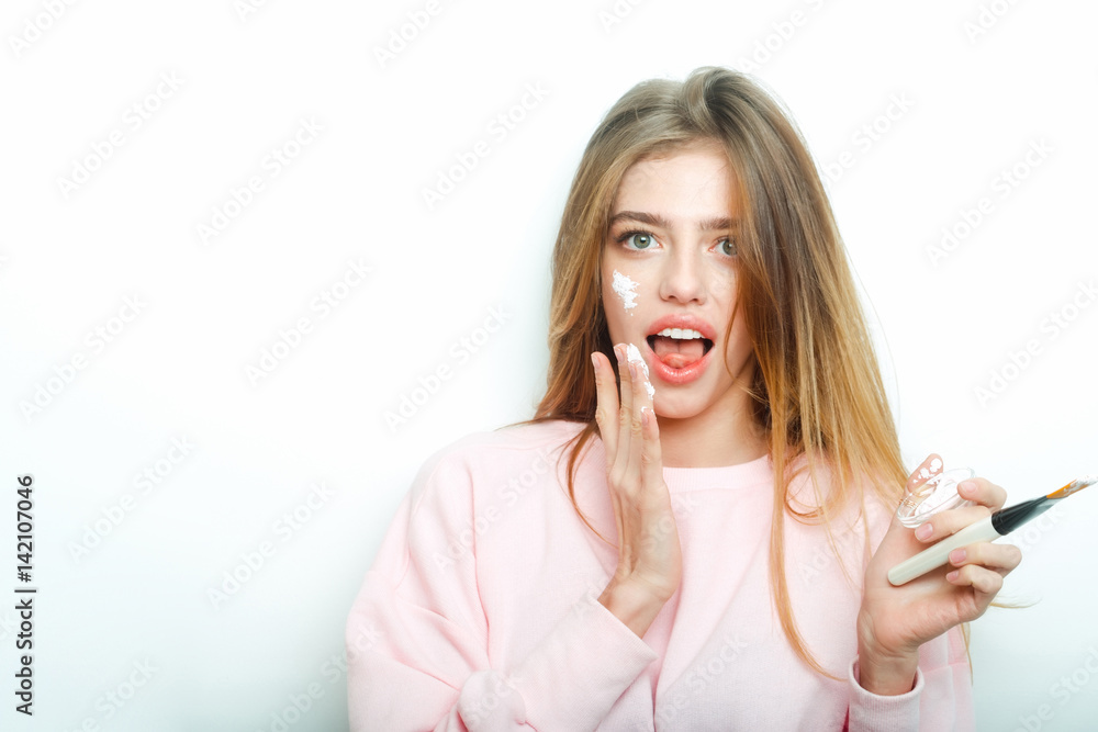 Surprised pretty girl putting facial cream or mask on face Surprised pretty girl putting facial cream or mask on face