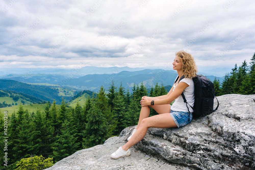 Naklejka premium A young woman stands on top of a mountain in cloudy weather enjoying the view