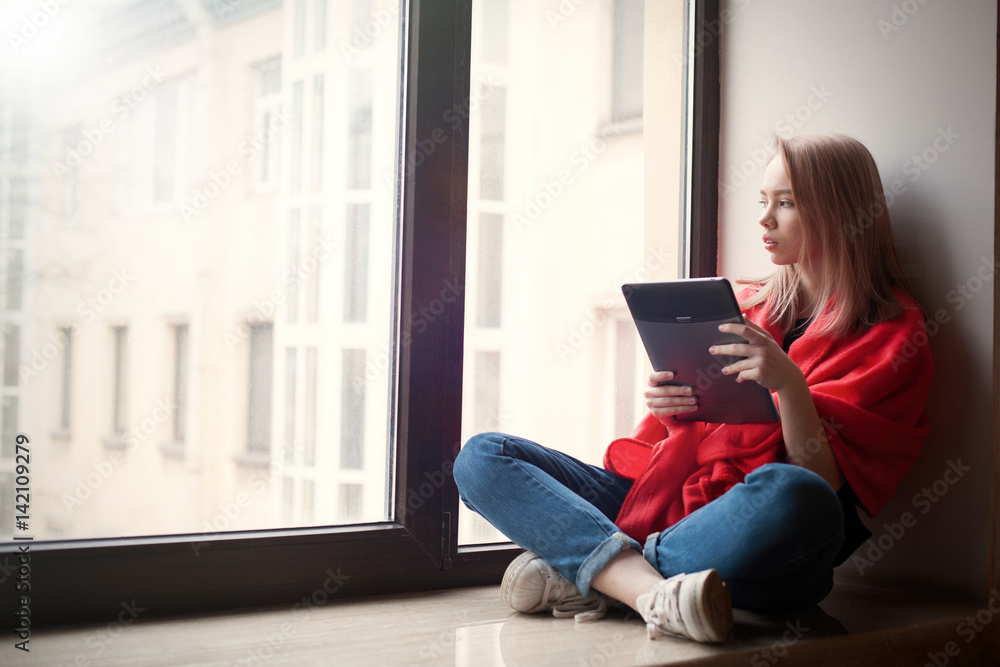 Portrait of a young girl reading an e-book at the window Portrait of a young girl reading an e-book at the window