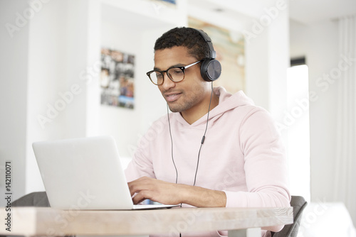 Enjoy music. Shot of a handsome young Afro American man using his laptop and listening music while working at home.
