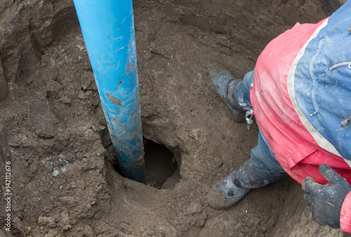 A worker stands near the blue pipe that sticks out from the Earth