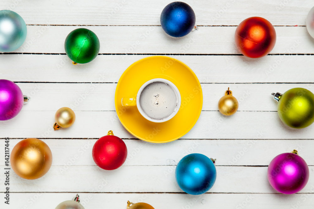 photo of yellow cup of coffee near colorful beautiful baubles on the wonderful white wooden background