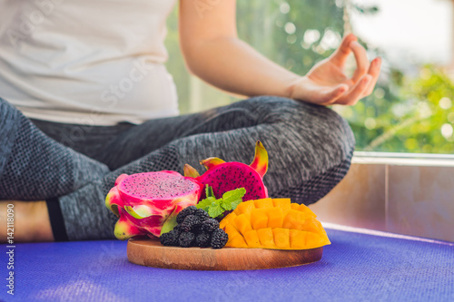 hand of a woman meditating in a yoga pose, sitting in lotus with fruits in front of her dragon fruit, mango and mulberry