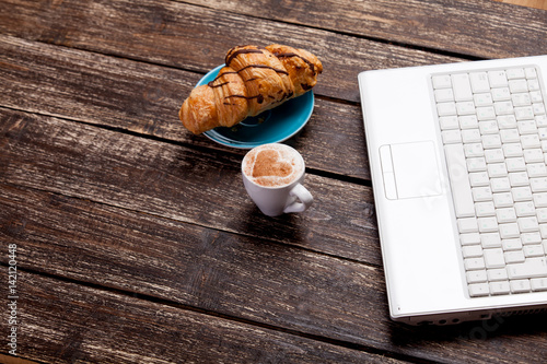 photo of delicious fresh croissant, laptop and cup of coffee on the wonderful brown wooden background