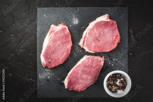 Fresh raw pork, steaks, on a cutting shale board on a black concrete table. Top view, copy space