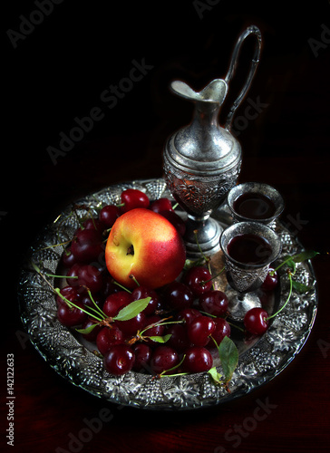 Still life with fresh cherries and a peach placed in silver plate on dark background. photo