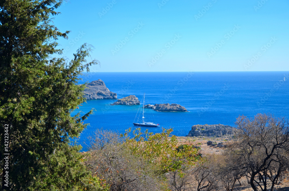 A view through the trees of the azure blue sea level in the bay in the Mediterranean sea with islands and mountains in the background under a clear blue sky