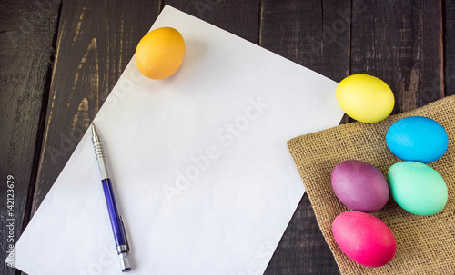 Colorful easter eggs with blank paper and pen on rustic wooden table . Ready to write a letter. Happy Easter
