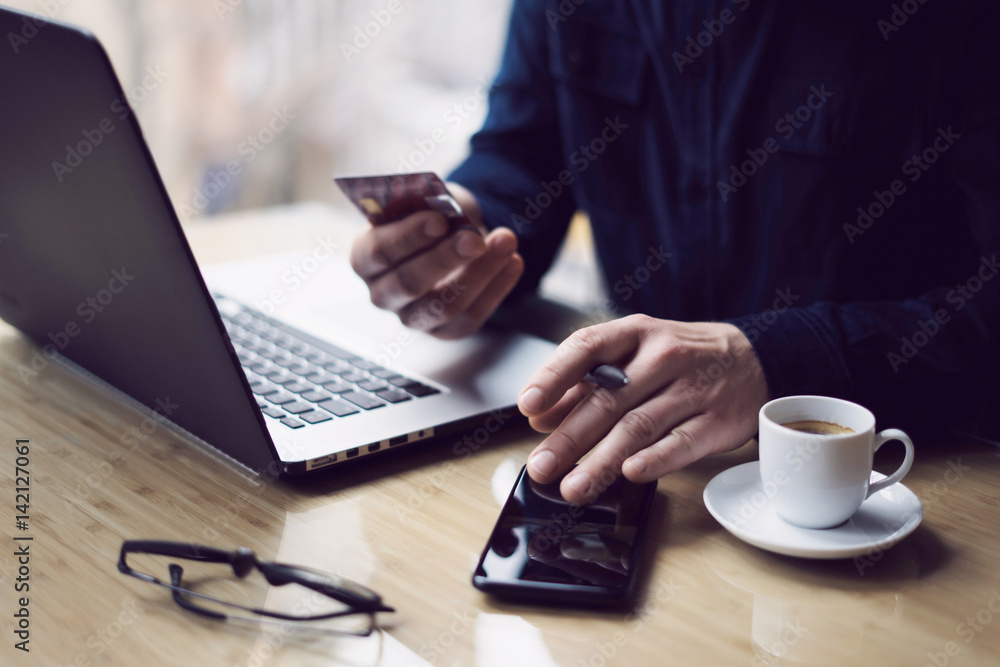 Businessman holding credit card in hand and using smartphone,laptop computer at the wooden table.Blurred background.Horizontal. Businessman holding credit card in hand and using smartphone,laptop computer at the wooden table.Blurred background.Horizontal.