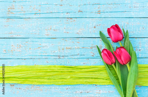 Fototapeta Naklejka Na Ścianę i Meble -  Frühling Blumen Strauss Tulpen pink auf Holz Hintergrund blau mit Geschenkband grün