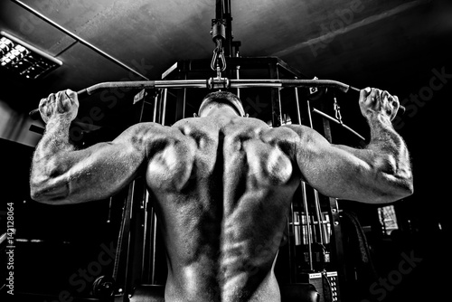 Fotografia Strong Bodybuilder Doing Heavy Weight Exercise For Back On Machine