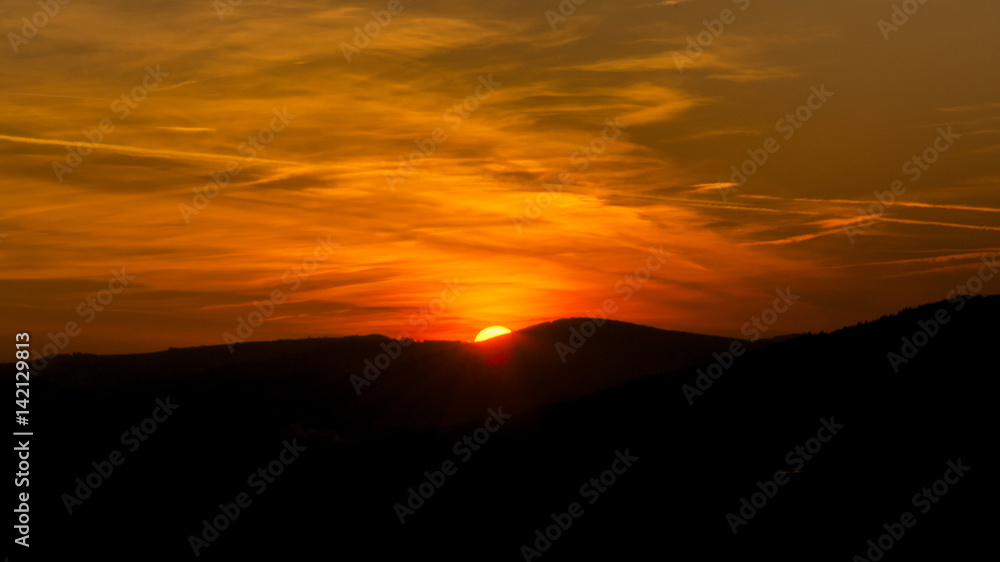 The sky is magenta and orange with alpenglow and clouds. Abstract red orange sky. Dramatic orange sky at the sunset background. The sundown behind hills.