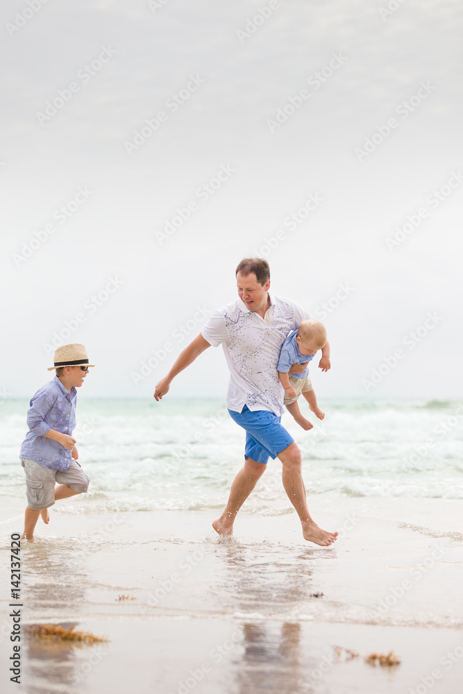 Portrait of father with two sons walking on the ocean beach. Summer vacations by the sea. Outdoors. Happy family. Portrait of father with two sons walking on the ocean beach. Summer vacations by the sea. Outdoors. Happy family.