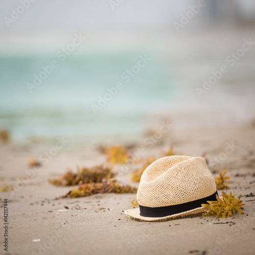 Nice straw hat laying on the sand. Beautiful ocean beach background. Outdoors. Vacation time. End of summer vacations. Dreaming of holidays by the sea. Traveling.