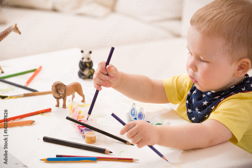 Cute little toddler boy in yellow shirt sitting at table and drawing with colorful paints. indoors. child having fun. Early learning. Creative. Toddler drawing. Cute little toddler boy in yellow shirt sitting at table and drawing with colorful paints. indoors. child having fun. Early learning. Creative. Toddler drawing.