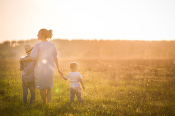 Beautiful young woman with two boys on the daisy meadow on a sunny day. Happy family on summer sunset. Kid boy, toddler and mom. Mum with baby and kid. Family and lifestyle concept
