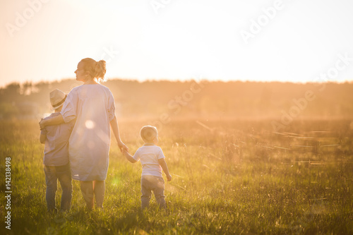 Beautiful young woman with two boys on the daisy meadow on a sunny day. Happy family on summer sunset. Kid boy, toddler and mom. Mum with baby and kid. Family and lifestyle concept