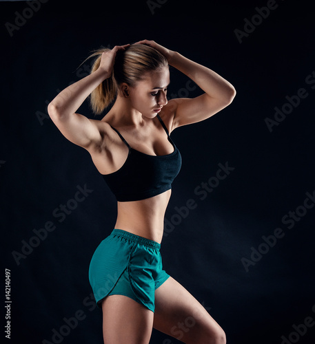 Sporty young girl in sportswear showing muscles on black background. Tanned young athletic woman. A great sport female body. © artyme