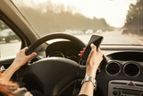 Female hands on the steering wheel of a car and hold a mobile phone. Photo in yellow colors.