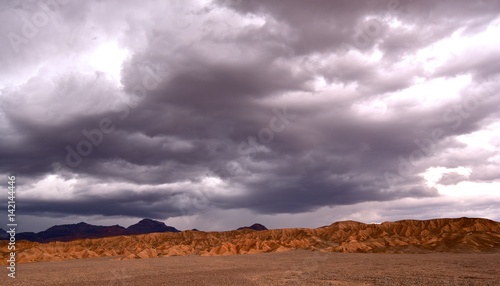 Vista of a red sandstone formation in Death Valley under a dark stormy sky.