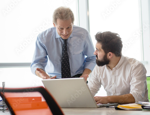 Mobbing, stress, work, scandal concepts. Angry boss man explaining his worker new business strategy while he is working on laptop computer.