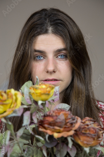 Portrait of a beautiful young white girl with blue eyes and brown hair holding a bouquet of dried flowers. She has a serious look and a little sad. 