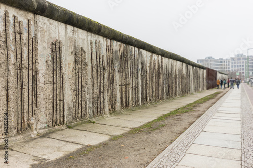Tourists taking pictures at the Berlin Wall memorial in Germany. Writing is visible on the cement wall. Two sides of the wall - East and West Berlin.