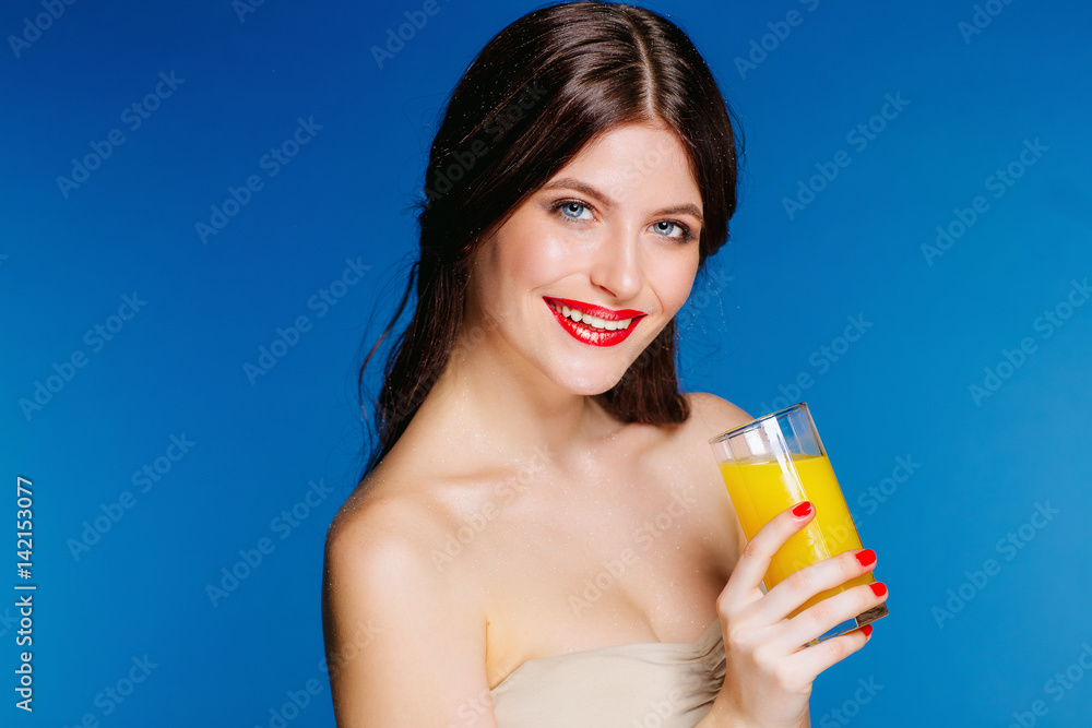Portrait of young Caucasian brunette girl smiling on a blue background in the Studio .Long hair makeover is drinking orange juice Portrait of young Caucasian brunette girl smiling on a blue background in the Studio .Long hair makeover is drinking orange juice