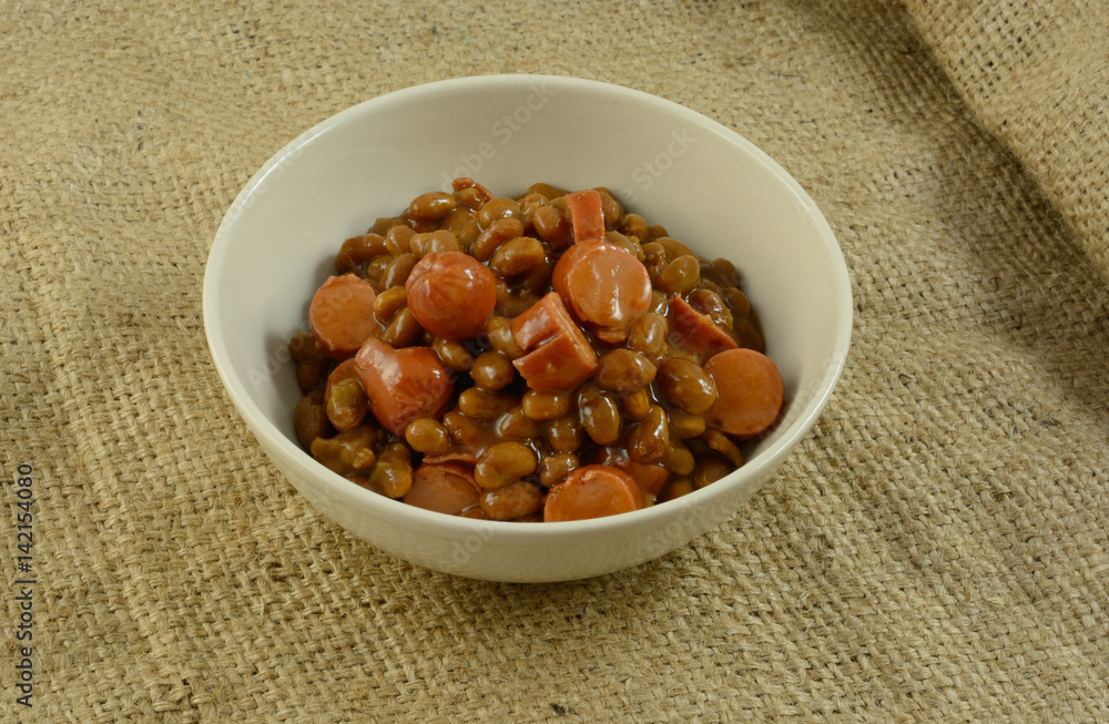 Sliced turkey hot dog frankfurters and baked beans in white bowl Sliced turkey hot dog frankfurters and baked beans in white bowl