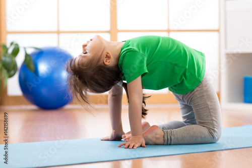 Child girl performing frog sportive execrcise in gym photo