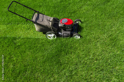 Lawn mower in the garden on green grass photographed from above