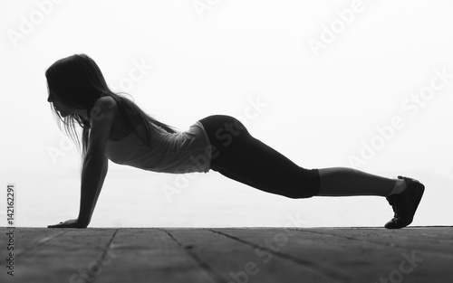 Black and white silhouette of beautiful young sporty woman is pressing on the floor