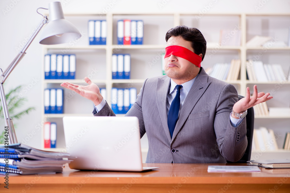 Blindfold businessman sitting at desk in office Blindfold businessman sitting at desk in office