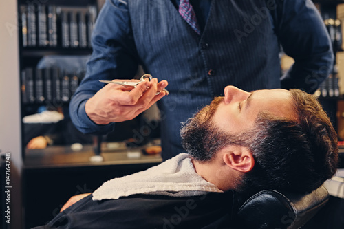 Stylish barber grooming a man's beard in a saloon.