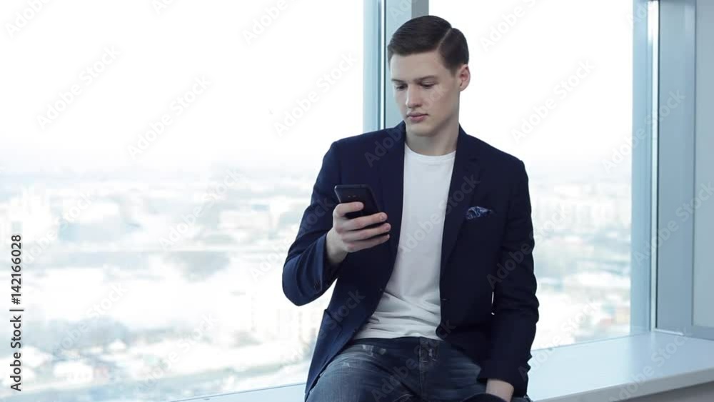 Good News From Friends in Social Networks/Young businessman is checking his social networks during the break. He is in the office with large bright windows. Lots of copy space Good News From Friends in Social Networks/Young businessman is checking his social networks during the break. He is in the office with large bright windows. Lots of copy space