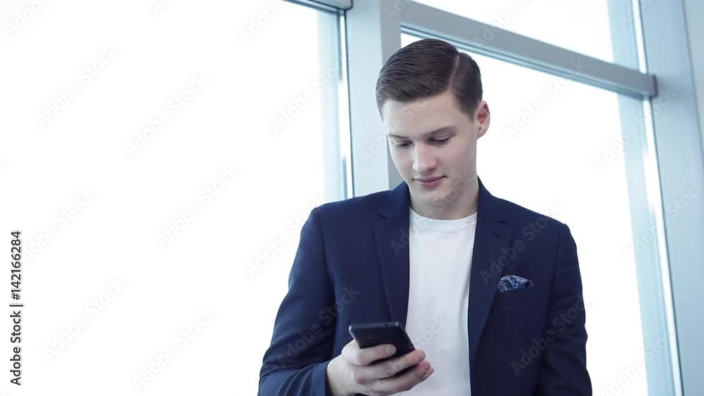 Good News From Friends in Social Networks/Close up of a young businessman checking his social networks during the break. He is in the office with large bright windows. Copy space Good News From Friends in Social Networks/Close up of a young businessman checking his social networks during the break. He is in the office with large bright windows. Copy space